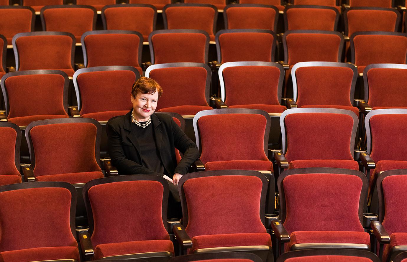 A woman sitting in a theatre, surrounded by red seats